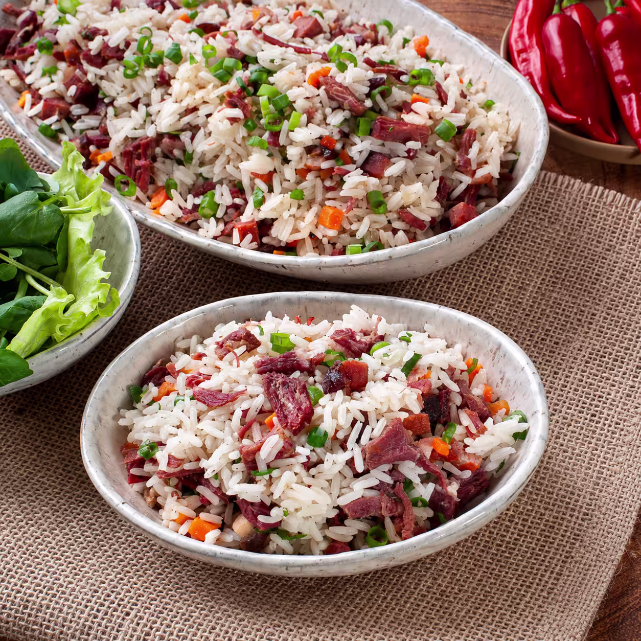 Two bowls of fluffy rice with tender shredded meat, carrots, and chopped green onions, served on a rustic burlap table.